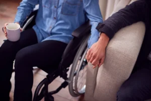 Disabled person in wheelchair holding hand of person sitting on couch